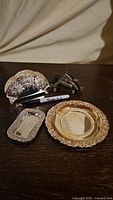 Photo showing the four items: two silver plated napkin holders in different sizes, a round silver plated wine bottle coaster, and a small rectangular stainless steel tray, along with a Sharpie pen for size reference.