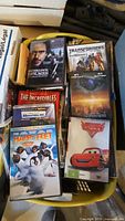 Box containing various DVDs including Sherlock Holmes, The Incredibles, Monsters, Inc., Happy Feet, Cars, and Transformers.