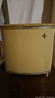 Front view of the gold metal hamper showing the ribbed texture and starburst emblem.