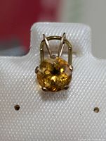 Front close-up of yellow round faceted gemstone pendant on a white earring card with visible 14 KT GOLD marking below.