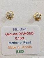 Front view of two 14K gold flower-shaped earrings with a center diamond and mother of pearl, alongside a product tag detailing material and carat weight.
