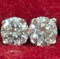 Close-up front view of both round brilliant diamonds set in white gold four-prong settings against red velvet background.