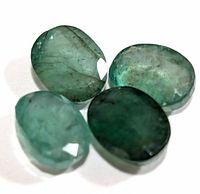 Four oval faceted emerald gemstones placed on a white background, showing different shades of green and typical internal inclusions.