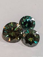 Three round cut loose genuine Moissanite stones showing brilliant multicolor internal reflections on a white background.