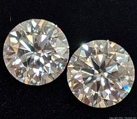 Two round cut moissanite stones on black background showing facets and clarity.