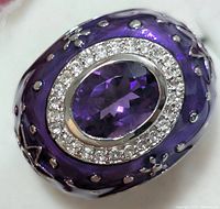 Close up front view of ring showing amethyst center stone and halo of small clear stones with purple enamel and silver decorative band.