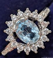 Close-up front view of ring showing oval blue topaz center surrounded by white topaz stones and part of the band embedded with stones.