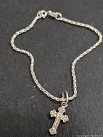 Full view of silver box chain bracelet with crucifix charm laid out on dark surface.