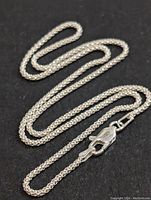 Full view of the silver chain necklace arranged in a loose wave showing the chain texture and clasp.