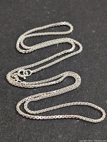 Full view of sterling silver box chain necklace arranged on black background showcasing entire length and smooth, reflective surface.