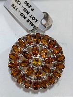 Close-up photo of round silver pendant with citrine gemstones in concentric circles, displaying the shape, color, and prong settings clearly.