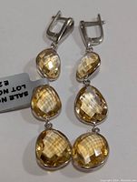 Pair of dangling silver earrings each set with three faceted citrine stones of oval and teardrop shapes in a warm yellow tone.