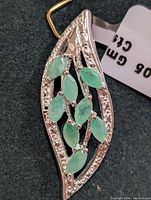 Leaf-shaped silver pendant with multiple marquise emerald stones and small clear stones along the border, shown from the front.