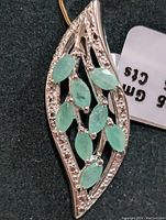 Close-up photo of silver pendant with seven marquise-cut green emerald stones inside a marquise-shaped silver frame adorned with small clear accent stones.