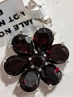 Close-up of the flower-shaped silver pendant with deep red garnet stones showing faceting and silver prong settings.