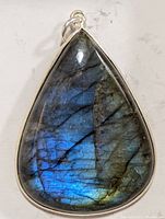 Close-up photo of the teardrop-shaped labradorite pendant with blue and green iridescence in silver setting.