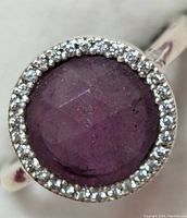 Close-up of the top of the ring showing the round ruby center stone surrounded by CZ stones in a silver setting.