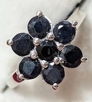 Close-up of ring top showing dark blue faceted sapphires in flower cluster set in silver prong setting.