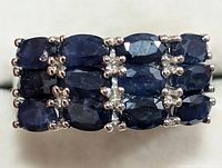 Front view of a sterling silver ring with three rows of faceted oval blue sapphires.