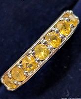 Close-up photo of yellow sapphire stones set in a silver band, showing round faceted gems in a shared prong setting.