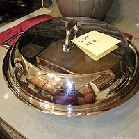Domed lid with polished surface reflecting surroundings, has a handle on top with a post-it note "Lot 44".