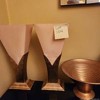 Two Art Deco style lamps with cream fabric shades and gold tone, angular bases next to a gold tone decorative vase.