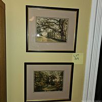 Two framed Wallace Nutting prints hung on a wall, matted and framed in similar dark wood frames with gold trim, showing serene landscapes.