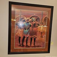 Framed artwork showing three women from behind in colorful dresses and hats with architectural arches in the background, matted and framed under glass.
