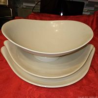 Stack of one white serving bowl and two platters on a red cloth background, showing shape and style.