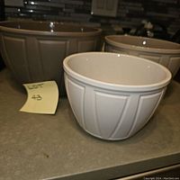 Three Crate & Barrel Carter mixing bowls in small, medium, and large sizes shown together on a kitchen counter. White ceramic with vertical ribbed design.