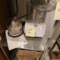 Photo of the assembled food processor base with attached processing bowl and food pusher, along with instruction manual on shelf.