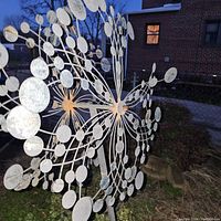 Side view of one metal wind spinner showing circular discs and structure with outdoor background.