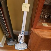 Full view of the Pur Steam Floor Steamer in room corner near wooden cabinet and fan.