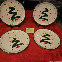 Four round ceramic plates with cream background, green rim, red dots and green stylized Christmas tree with star design
