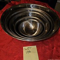Five stainless steel mixing bowls nested from largest to smallest on a red fabric background with a lot number tag in front.