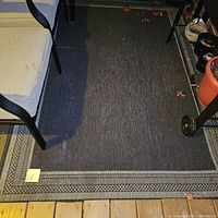 Rug fully displayed on porch between porch railing and chair, showing the dark gray central area and patterned border