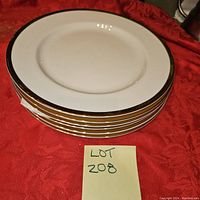 Stack of 6 white plates with gold trim on a red fabric background.