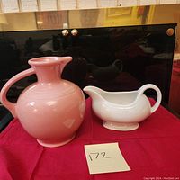 Front view of pink pitcher and white gravy boat placed on a red cloth with a note showing lot number 172.