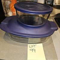 Two Pyrex glass storage containers stacked, both with blue lids, showing condition and size comparison.