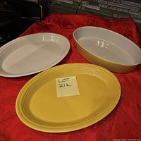Three ceramic serving platters displayed on red cloth, two oval platters in yellow and white, one rectangular deep platter in off-white with yellow trim.