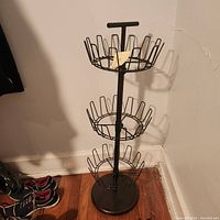 Full view of the three-tier, black metal shoe tree rack standing on wooden floor, showing wire compartments for holding shoes.