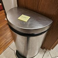 Front angle view of Simplehuman stainless steel pedal step trash can with top lid closed. Shows the semi-round shape and surface finish.