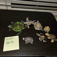Seven assorted turtle figurines displayed on a dark surface with a note saying Lot 214.