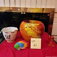 Photo of all four items on red cloth: heavy glass vase, ceramic butterfly pot, colorful wooden fish, amber glass tulip figurine