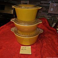 Stacked view of three yellow Pyrex mixing bowls with glass lids showing exterior and pattern on two bowls