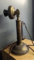 Side view of antique brass and Bakelite candlestick telephone showing mouthpiece and silk cord.