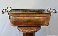Front and top view of the rectangular copper jardiniere showing the aged patina and blue Delft porcelain handles on either side.