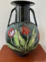 View of vase front showing raised red tulip decorations with green leaves on blue background and black neck and handles.