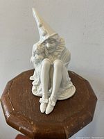 Front view of Rosenthal porcelain figurine showing seated Pierrot clown holding dog, white glazed porcelain, set on wood stand.