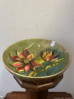 Front-angle image of the Moorcroft bowl showing two large hand-painted red and yellow flowers with green leaves on a green background.